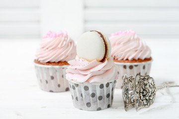 Homemade vanilla cupcakes with cream cheese cap and macaroon on a wooden background. Selective focus.