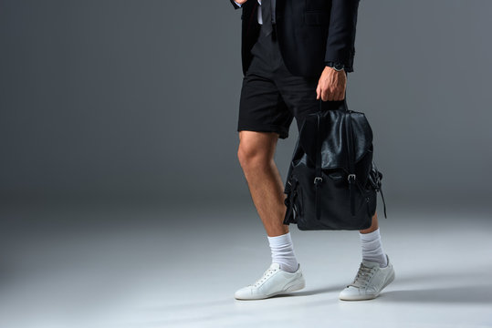 cropped image of stylish man in shorts holding backpack on grey background