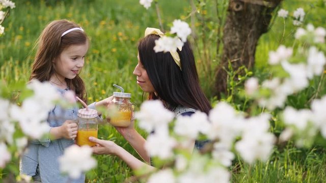 Mom with a little daughter drink orange juice in the spring garden. In the hands of a bottle with straws and orange juice