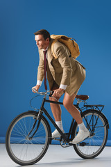 focused man with backpack riding bicycle and looking away on blue