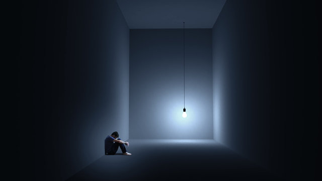 Ein Mann sitzt depressiv in einem Raum mit einer Gl&uuml;hbirne