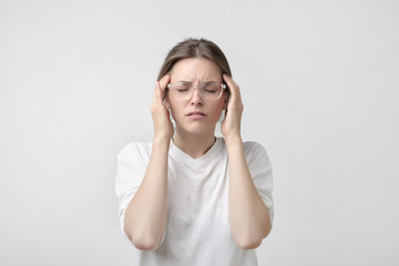Fototapeta premium European girl in white t-shirt suffers from terrible headaches and compresses the head with fingers.