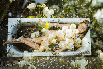 Celebration concept.  The flowering of the garden. Flowers fall on the naked body of a young beautiful girl. Young spring fashion woman in spring garden.  - obrazy, fototapety, plakaty