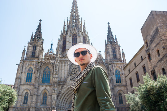 A young guy, a tourist, stands in front of the facade of The Cathedral of the Holy Cross and Saint Eulalia in Barcelona, Spain