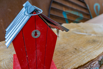 Tiny red house, maybe a bird house standing on a piece of wood with a old rusty cooking grid in the background. Seemed like leftovers from a garage sale turned into bulky waste.