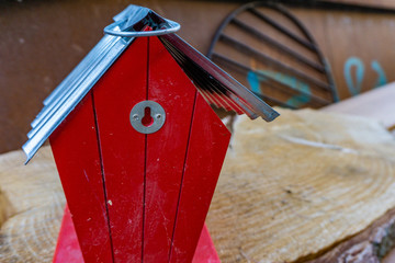Tiny red house, maybe a bird house standing on a piece of wood with a old rusty cooking grid in the background. Seemed like leftovers from a garage sale turned into bulky waste.