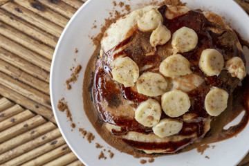 Banana chocolate pancake top view photo. Pancake breakfast on wooden table. Banana chocolate dessert flat lay.