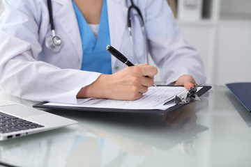 Fototapeta premium Doctor woman filling up medical form while sitting at the table, close-up of hands