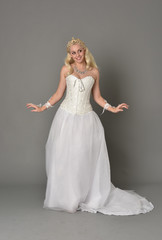 full length portrait of blonde girl wearing white corset gown. standing pose on grey studio background.