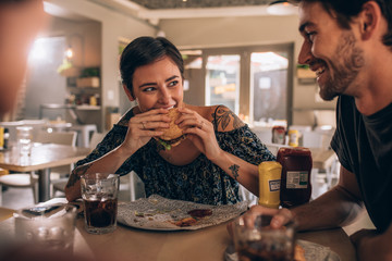 Woman eating burger with friends at restaurant