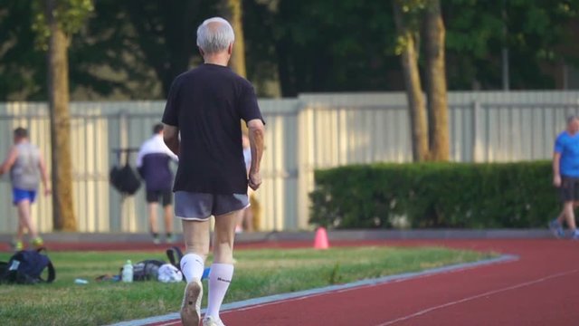 Old man jogging around the stadium. Back view. Slow motion