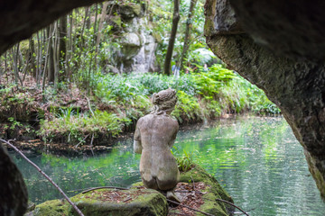 Statue of back nude woman seen from behind, facing small lake surrounded by green luxuriant vegetation, at Reggia di Caserta Naples Campania Italy. - obrazy, fototapety, plakaty