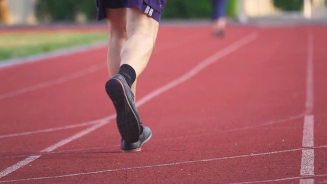 Low angle shot of an senior man's legs jogging on the stadium. Back view. Slow motion