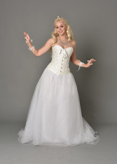 full length portrait of blonde girl wearing white corset gown. standing pose on grey studio background.