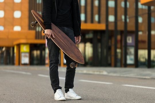 Man hipster holding skateboard or long board outdoors, cropped image. Leisure, healthy lifestyle, extreme sports 