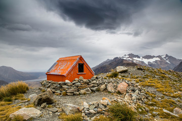 Mountain shelter red cabin high on a mountain side under stormy clouds
