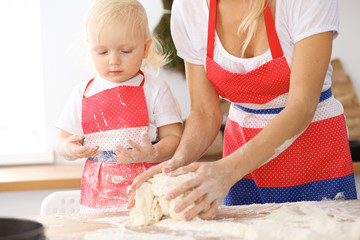 Little girl and her blonde mom in red aprons  playing and laughing while kneading the dough in the kitchen. Homemade pastry for bread, pizza or bake cookies