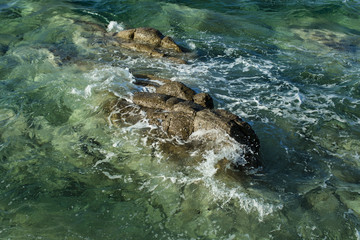 Sea waves wash stones. Sea or ocean water with foam and ripples. Rock in transparent water. Travelling and travel. Summer vacation and wanderlust