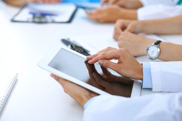 Doctor using tablet computer at medical meeting, closeup. Group of colleagues at the background