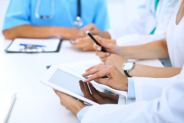 Doctor using tablet computer at medical meeting, closeup. Group of colleagues at the background