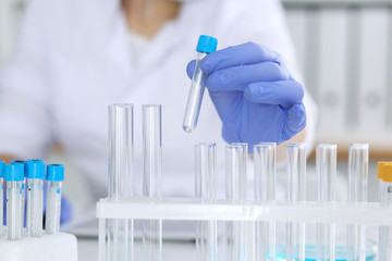 Close-up of professional female scientist in protective eyeglasses making experiment with reagents in laboratory. Medicine and research concept