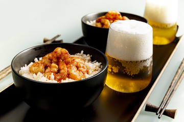 Fried shrimp and rice in a black bowl. Glass with beer. The background is gray.