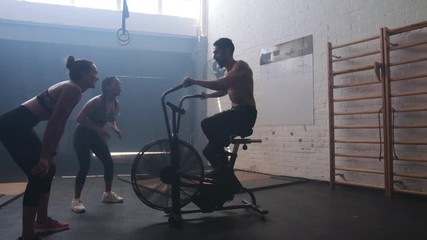 Man exercising on air bike in gym with friends
