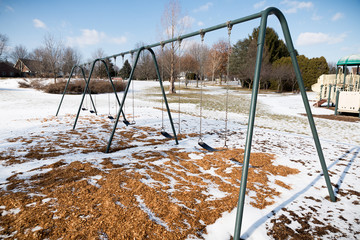 Swings in playground with snow in the middle of winter and no one sitting on benches 