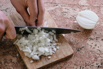 Man gently cuts the onion into small pieces and takes a wooden board with onion from the table. Close-up hands.