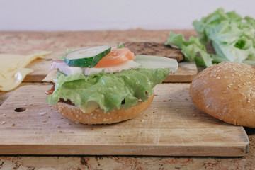 Products for preparation of burgers: buns, cutlets, cheese, salad, on the table. Side view.