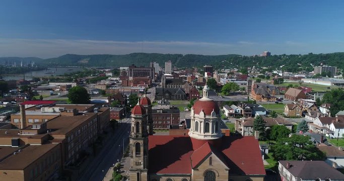 A slow forward aerial establishing shot (DX) of the small rust belt Ohio town of Steubenville. St Peter Church in the foreground. Barges on the Ohio River in the distance.  	