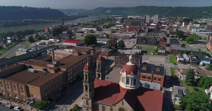 A high slow forward aerial establishing shot (DX) of the small rust belt Ohio town of Steubenville. St Peter Church in the foreground. Barges on the Ohio River in the distance.  	