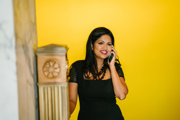 An image of a successful and attractive Indian Asian woman talking to someone over the phone while climbing up the stairs to get to her office. She is wearing a very elegant professional black dress.