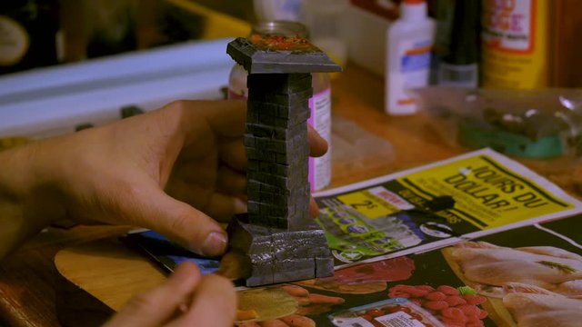 Close up of a hand applying wash to miniature painted pillar.