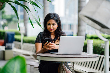 A confident and successful Indian woman (professional or business woman) is sitting and working on her laptop in the day. 