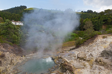 Hot spring surrounded by volcanic terrain and mountainous landscape in Furnas, Azores, Portugal. Summer landscape of Azorean village on a cloudy day.