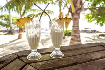 Half full glasses of tropical pina colada cocktail drink with pineapple garnish in glass with straws at exotic beach at Lefaga, Upolu Island, Samoa, South Pacific