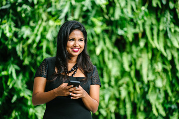 A portrait of a young Indian Asian woman sending an SMS on her mobile phone. She looks fulfilled after a long day at the office.