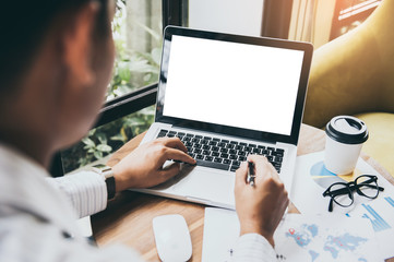 Business man hands holding pen and using laptop with blank screen on desk in cafe.