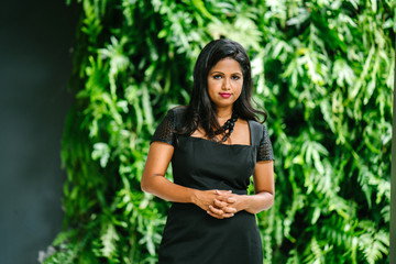 A portrait of an Indian Asian female professional striking a very elegant pose in front of the camera. She is smiling and looks very confident and sophisticated in her black dress.