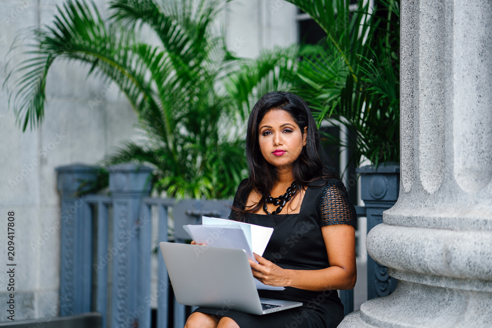 Wall mural a mature and confident indian asian woman sits on the steps of a legal looking building and is worki