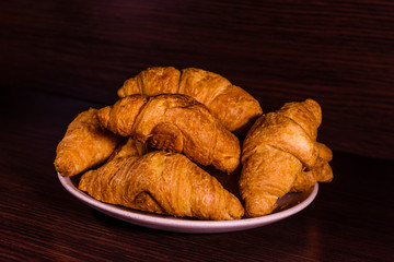 Plate with fresh croissants on a dark wooden table