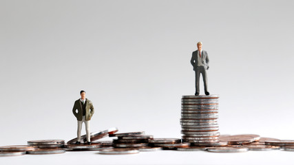 Miniature people standing on a pile of coins.