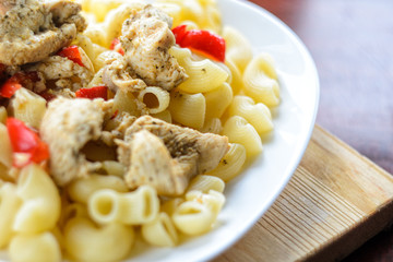 Hot Pasta with Chicken Breast Meat and Vegetables in Large White Plate on Wood Table, Close-Up. Food Background