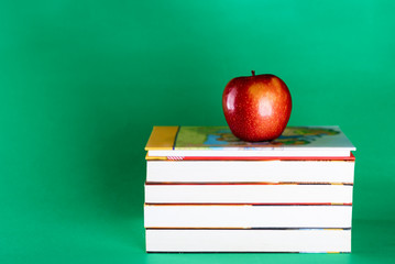 New textbook and red apple on green background. Concept Back to College, prepare to school returning to learn after summer holidays.Copy space for text.