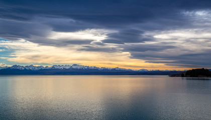 Calm lake scene at sunrise with snow capped mountains behind