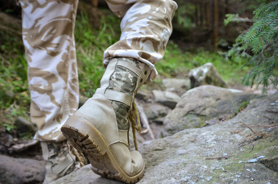Close up of a military man in trekking shoes going on a rocky path in the forest. 
