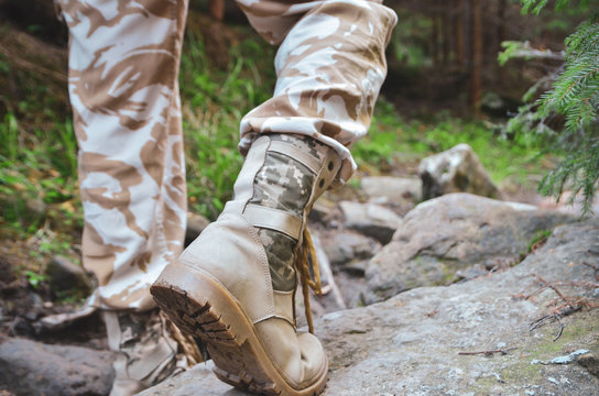 Close up of a military man in trekking shoes going on a rocky path in the forest. 