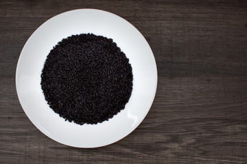 Raw black rice on a white plate on a wooden table. Healthy diet food