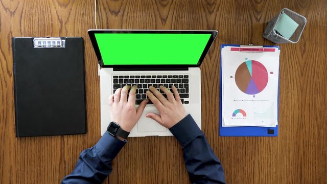 Businessman hands typing and scrolling on a laptop with green screen. Top view footage